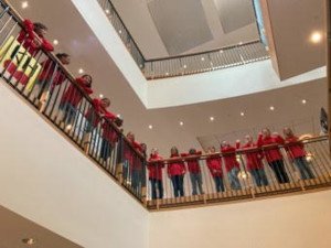 A group of people in red shirts looking down from a balcony.