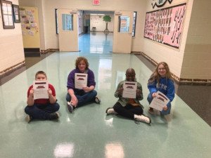 A group of kids siting on a floor holding certificates.
