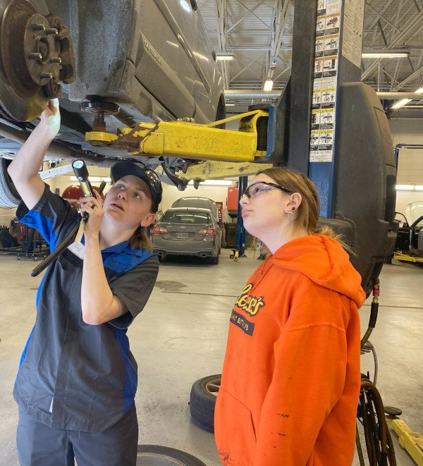 A mechanic showing a young woman the mechanics of a car.