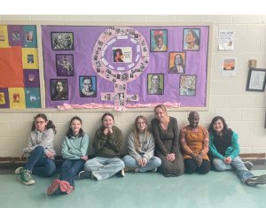 A group of people seated against a wall and smiling.