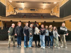 A group standing on a theater stage with their back to the seats.
