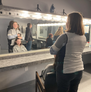 A woman stying a girl's hair in the dressing room of a theater.