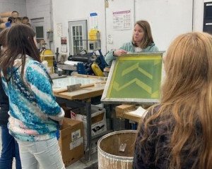 A woman showing students a silkscreen