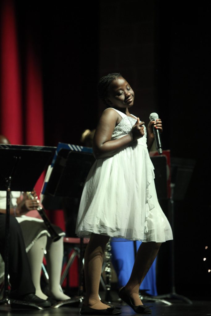 A girl on stage in a white dress holding a microphone.