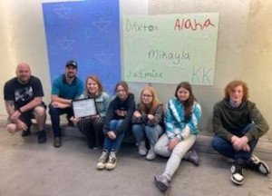 A group of people seated against a blue and white wall.